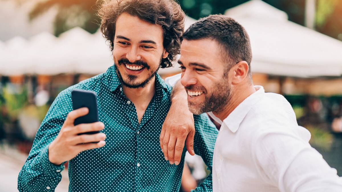 Two friends smiling as they stand outside and look at one of the friends' phones.