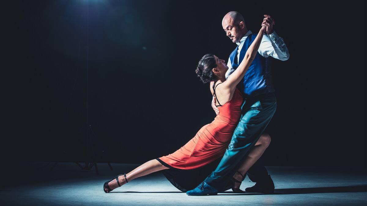 Two ballroom dancers under a spotlight in a dramatic pose.