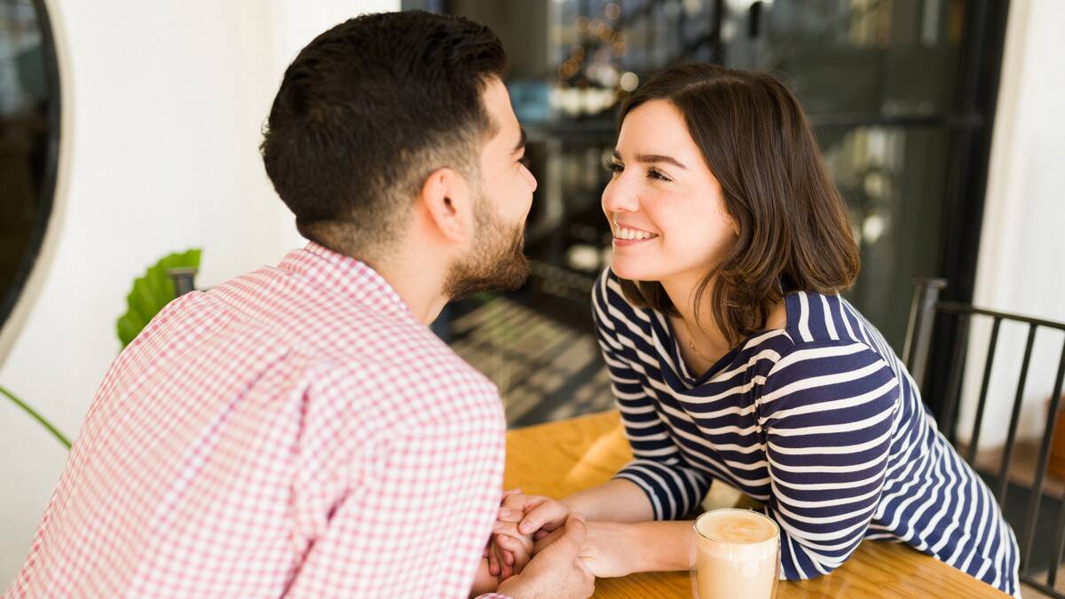A couple leaning across a table to look into each other's eyes as they smile, holding hands.