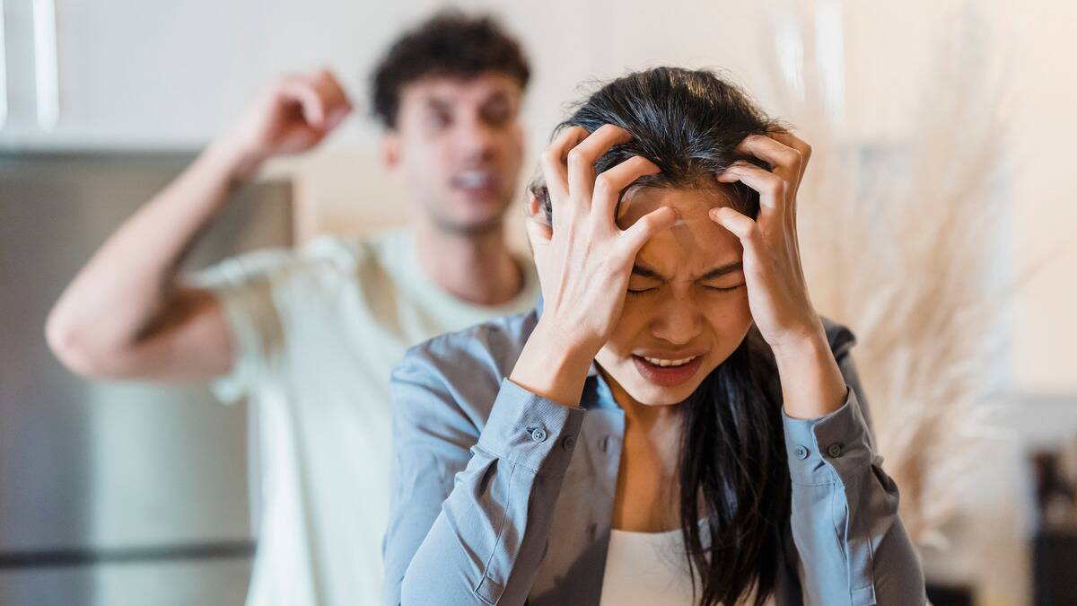 A woman clutching her head in frustration, a man seen yelling behind her.