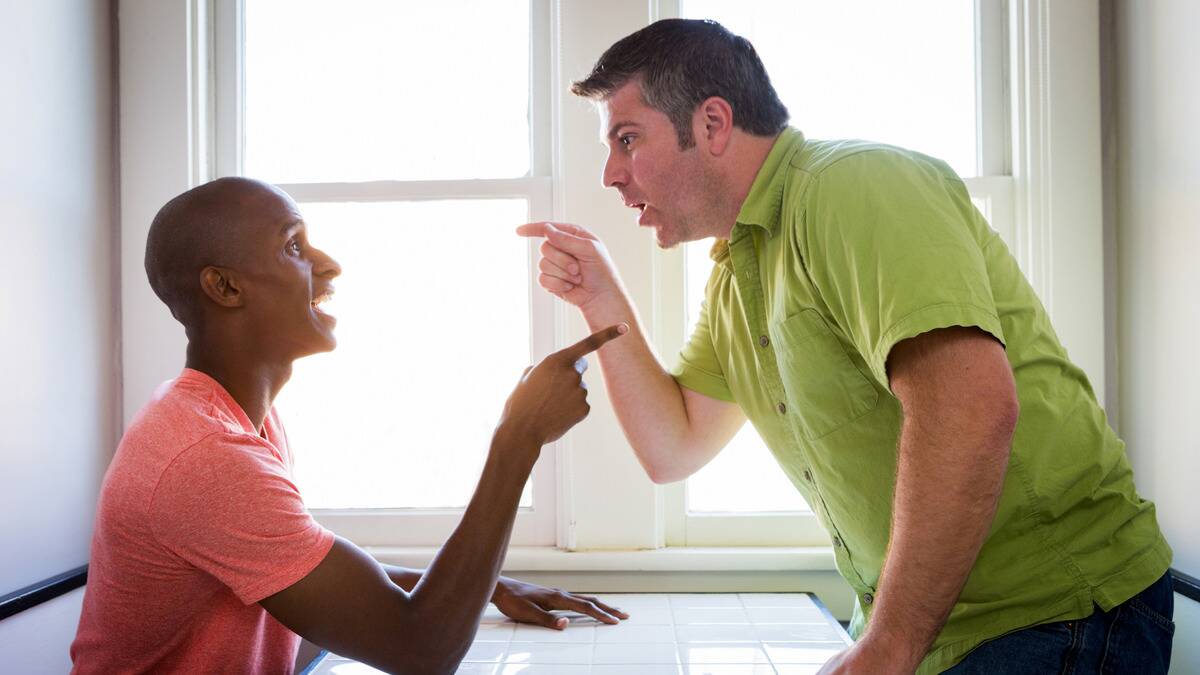 Two man pointing at each other in an argument, one sitting, one standing.