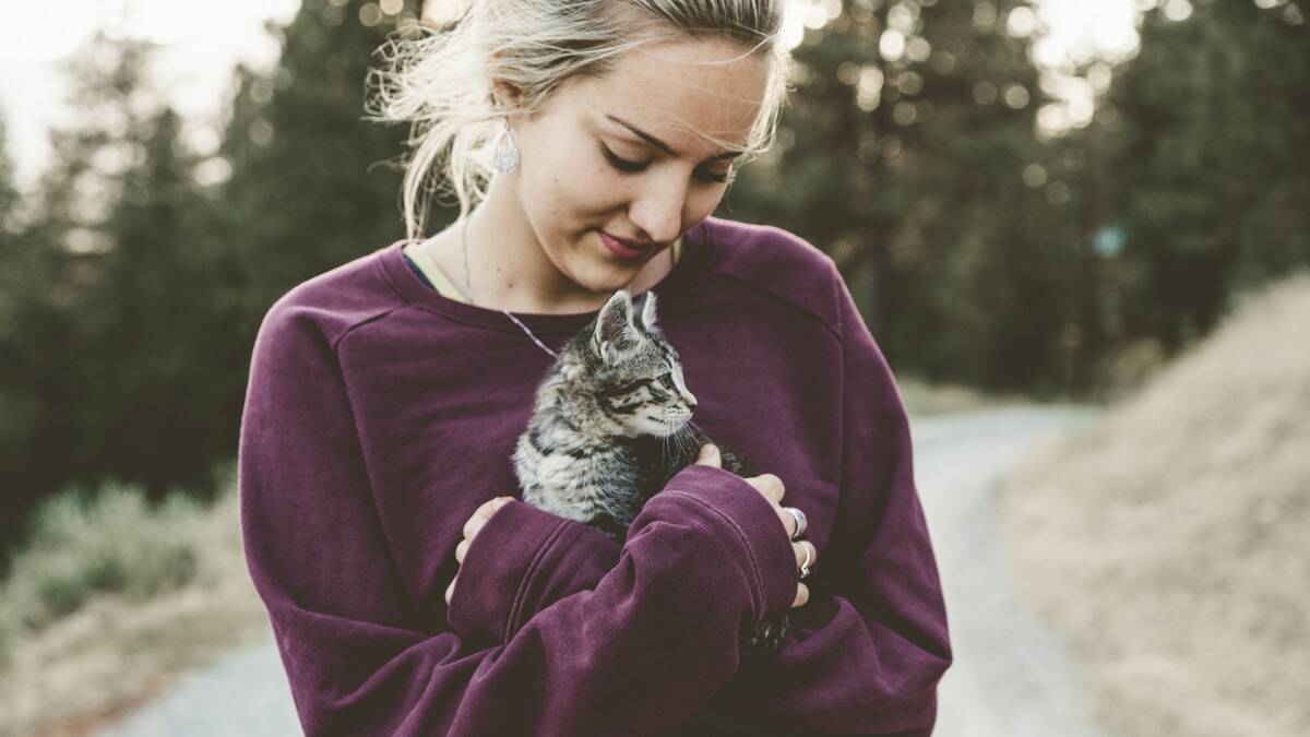 A woman holding a kitten in her arms close to her chest, looking down and smiling at it.