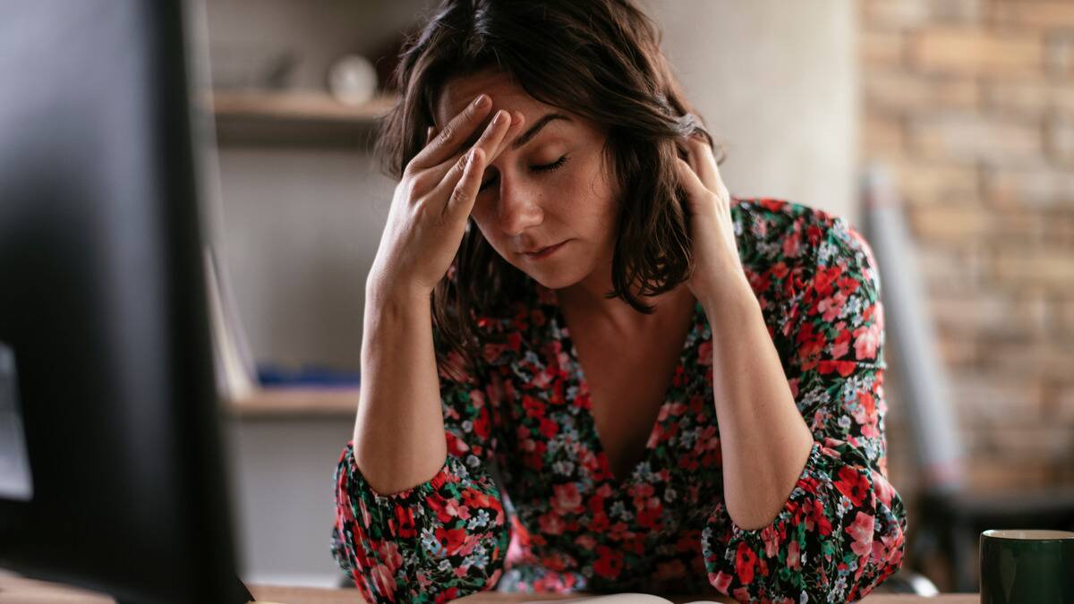 A woman sitting at her desk with her hand on her forehead, seeming pained or annoyed.