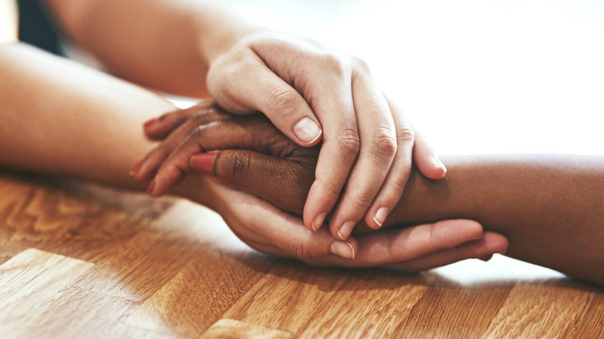 A closeup of someone using both hands to cradle one of someone else's hands in a comforting gesture.