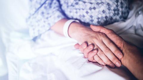 A close shot of someone holding hands with a person in a hospital bed.