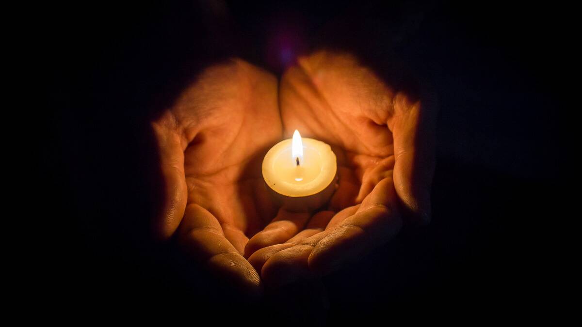 An above shot of a pair of hands cupping a lit tealight candle.