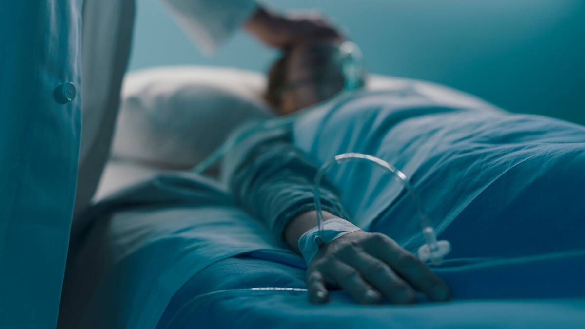 Someone laying in a hospital bed, a doctor placing a hand on their forehead, the shot focusing on the patient's hand.