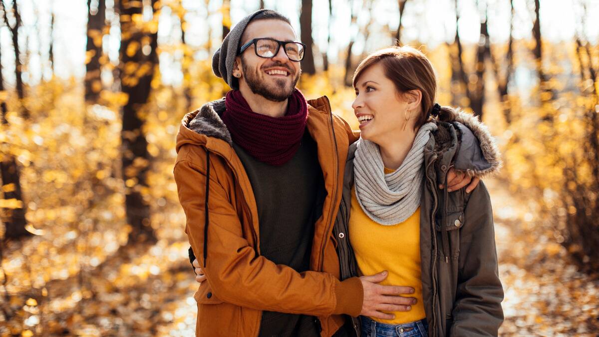 A couple walking through an autumn path, the man's arm around his girlfriend.