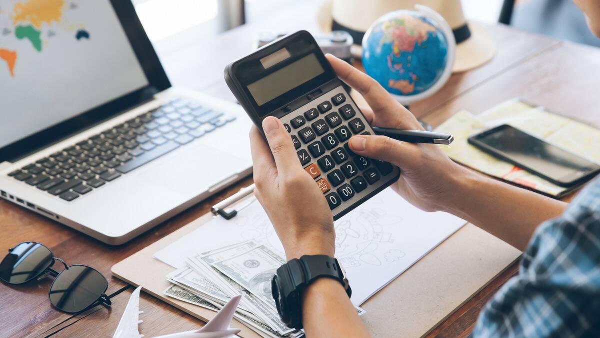 An over the shoulder shot of someone punching numbers into a calculator, money seen on the desk beneath them.