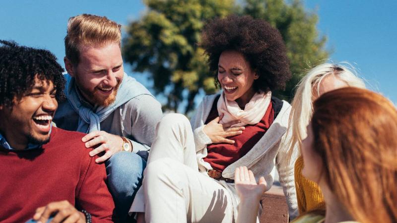 A group of friends all sitting together outside, laughing as they chat.