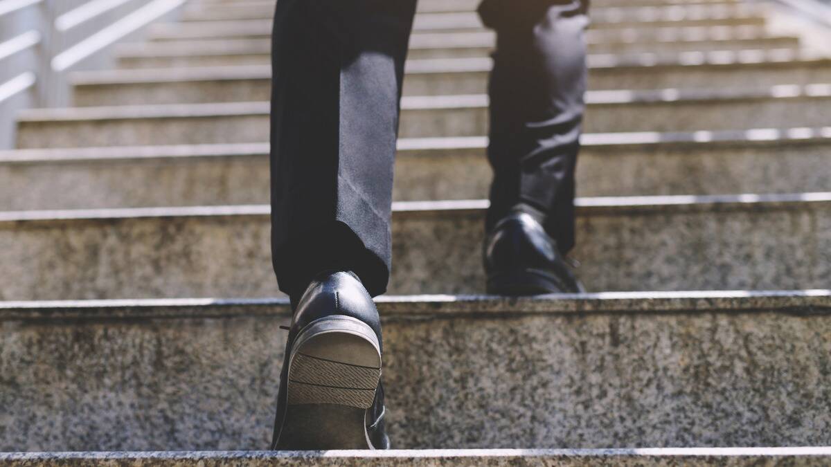 A low and close shot of someone in dress shoes walking up a set of outdoor stairs.