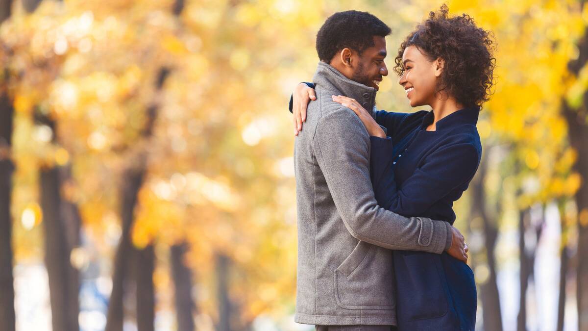 A couple standing outside, smiling as they look into each other's eyes, arms around each other.