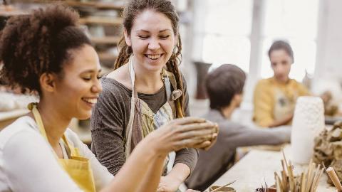 Two women at a pottery class, smiling as they sculpt things.