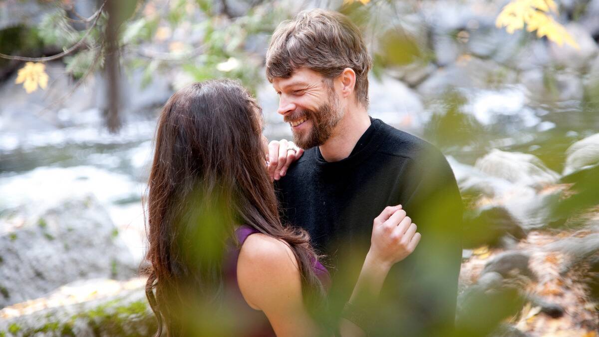 A couple embracing and smiling at one another, seen through the branches of a tree.
