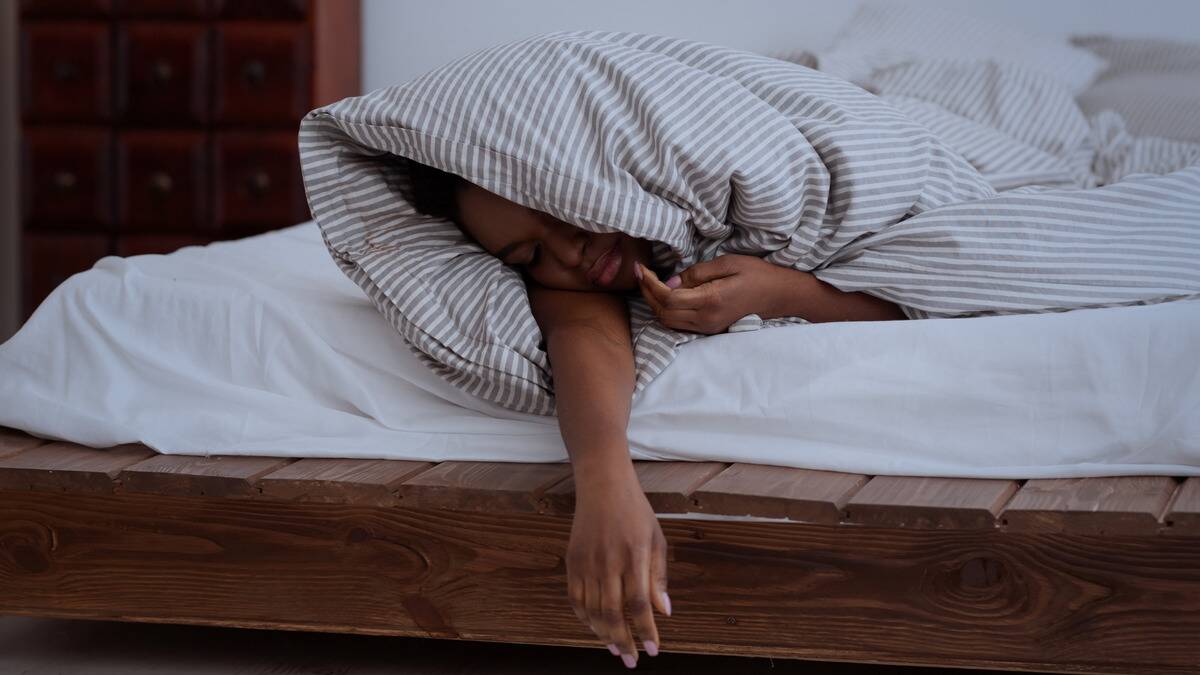 Someone sleeping wrapped in a blanket, arm hanging off the bed.