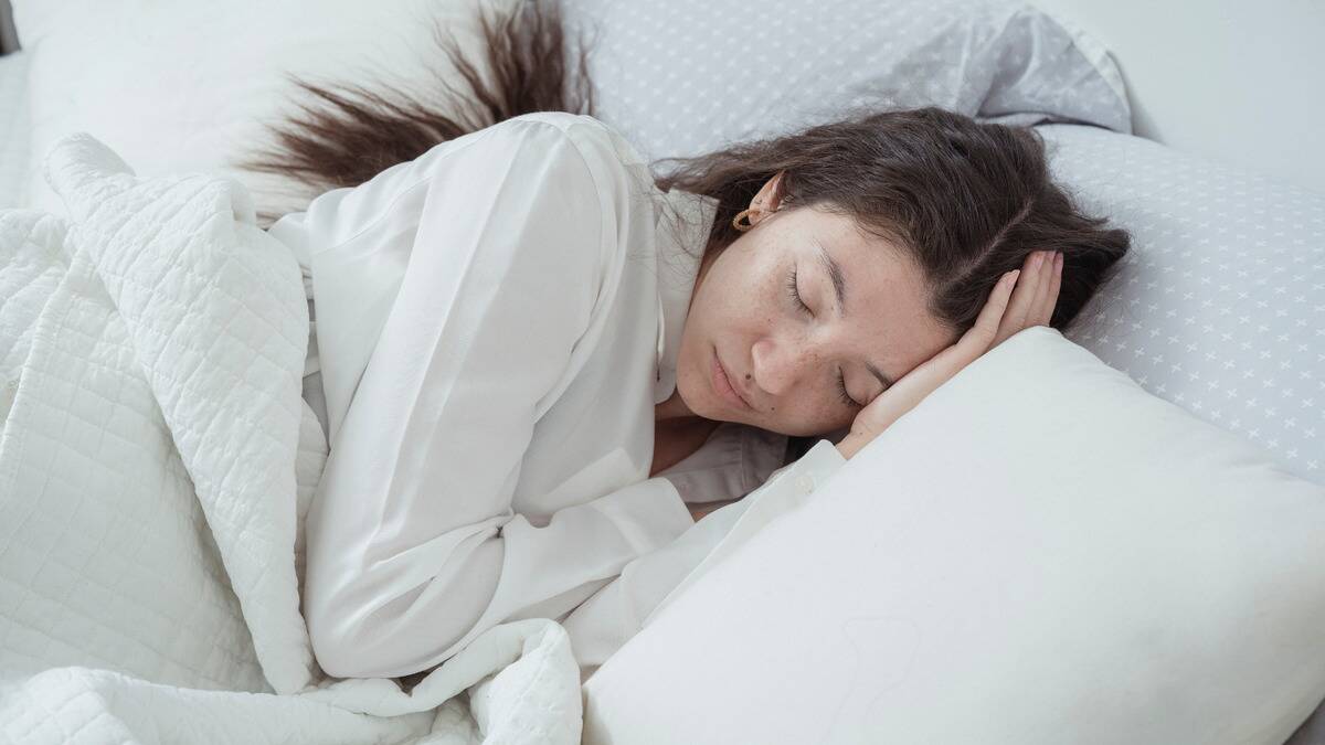 A woman asleep in bed, hands under her head.