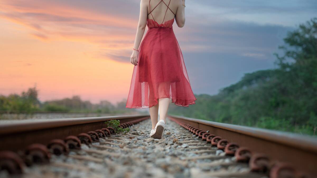 A woman walking down some railroad tracks during a sunset.