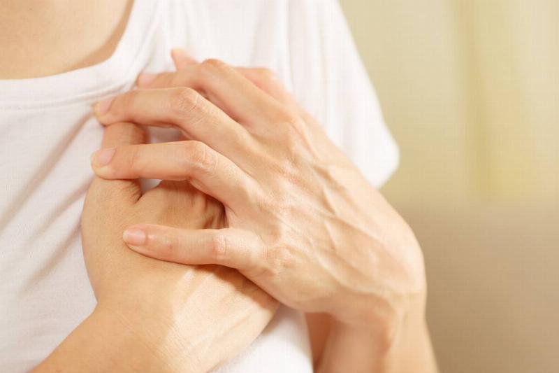 A close shot of someone with both hands over their heart, lightly grabbing at their chest.