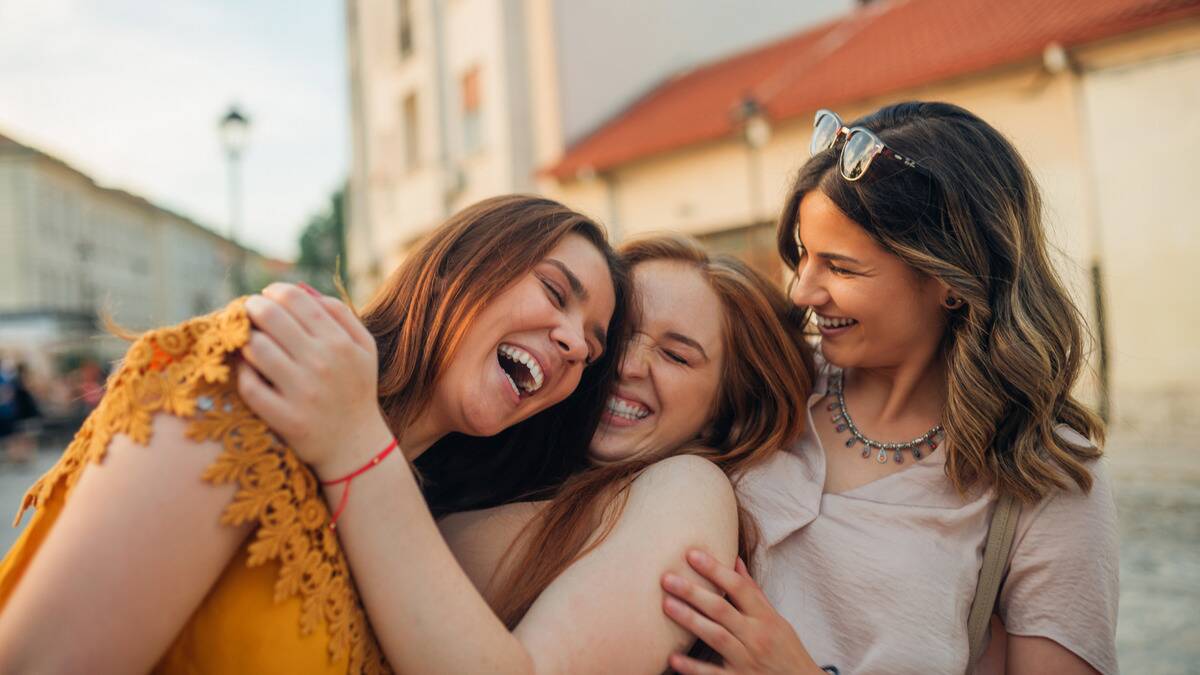 Three friends close to each other, leaning into one another, laughing together.