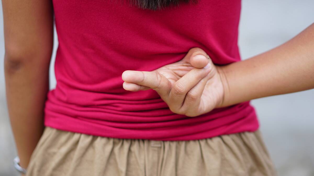 A close shot of a woman crossing her fingers behind her back, indicating lying.
