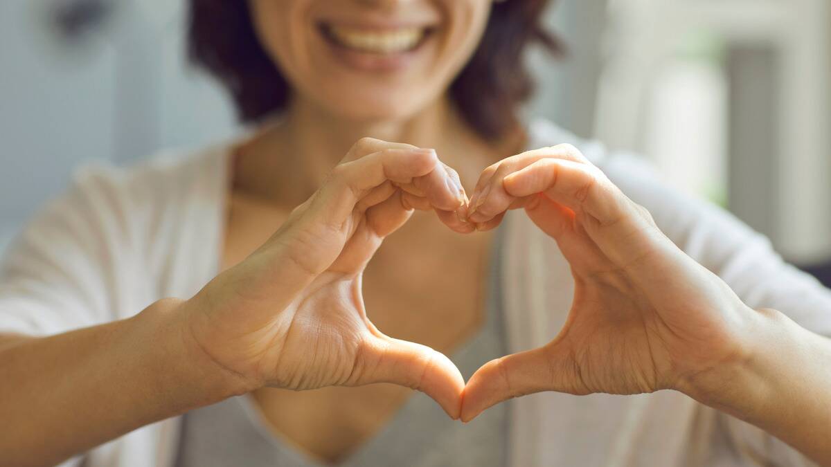 A woman smiling as she makes a heart shape with her hands.