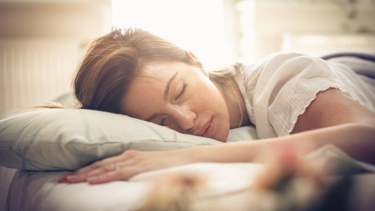 A woman sleeping in bed, camera focused on her face, the morning sun shining on her.