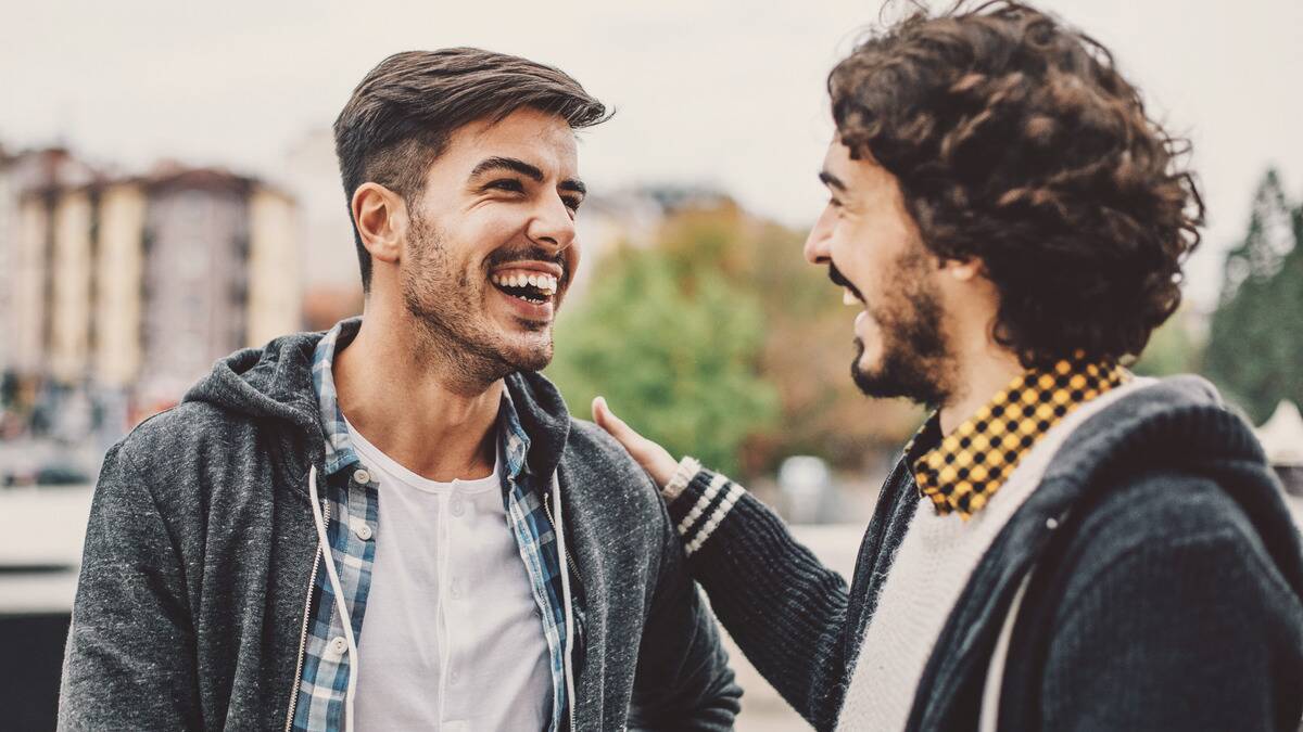 Two friends smiling and laughing, one of them putting his hand on the others shoulder.