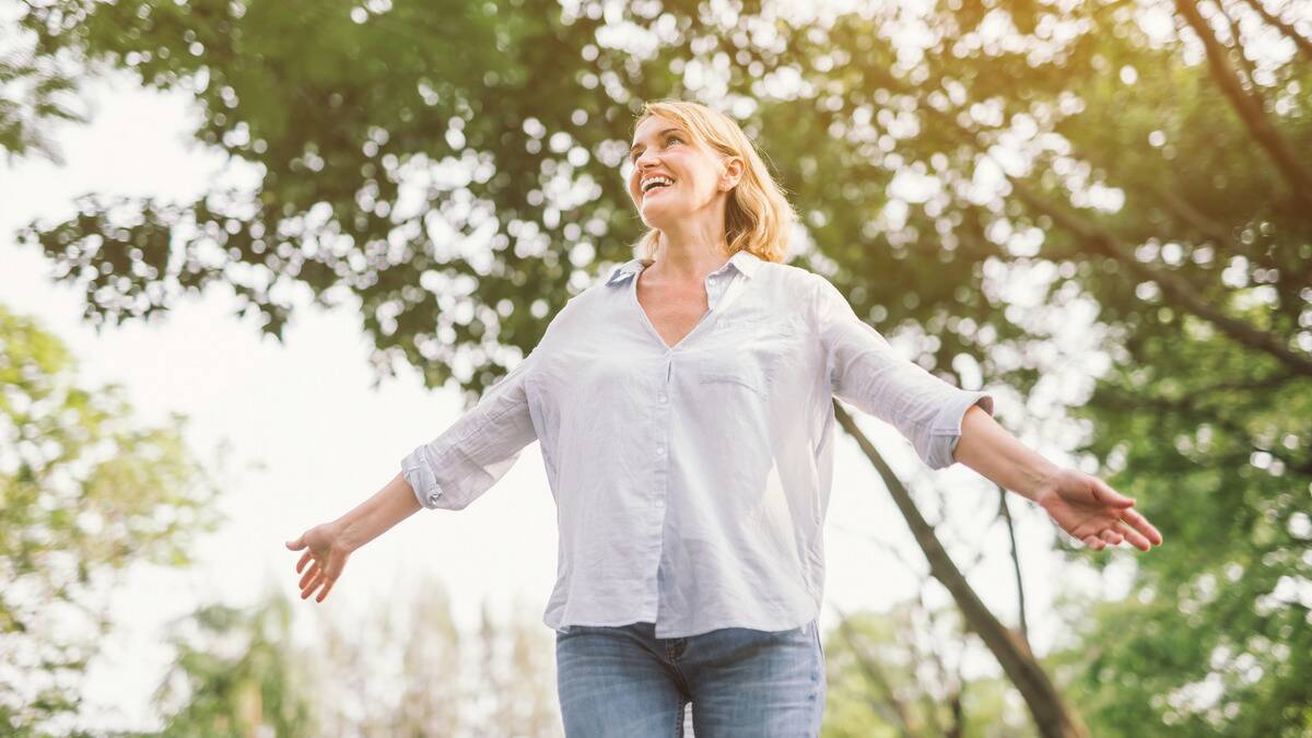 A woman with her arms out as she walks outside, smiling as she looks to the sky.