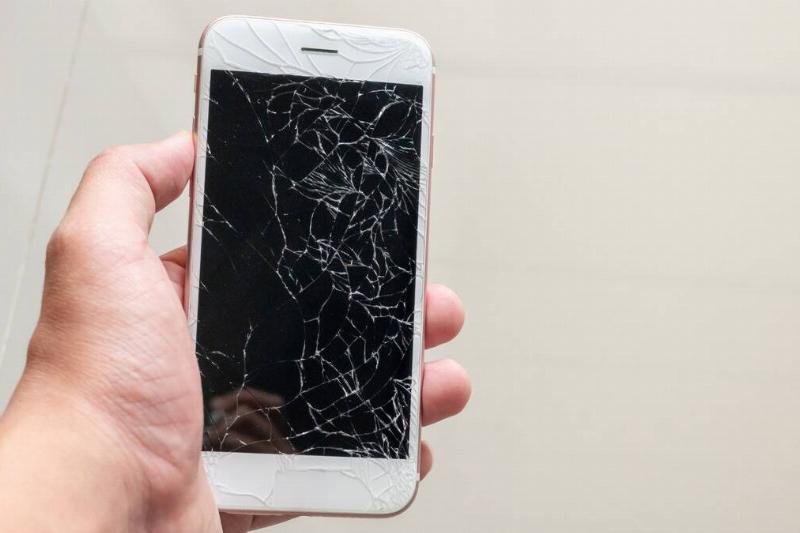 A hand holding a phone with an extremely cracked screen.