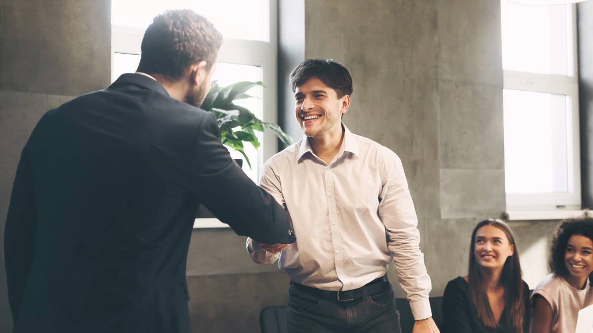 A man and his boss shaking hands as he's being given a promotion.