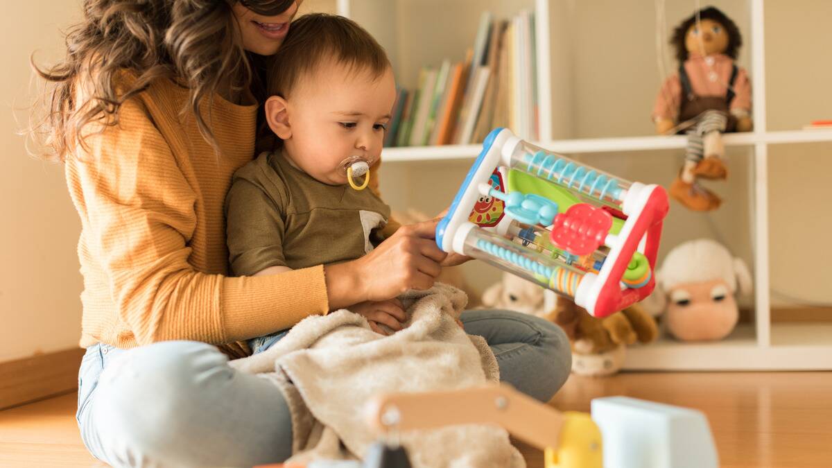 A woman holding her baby in her lap, playing with him.