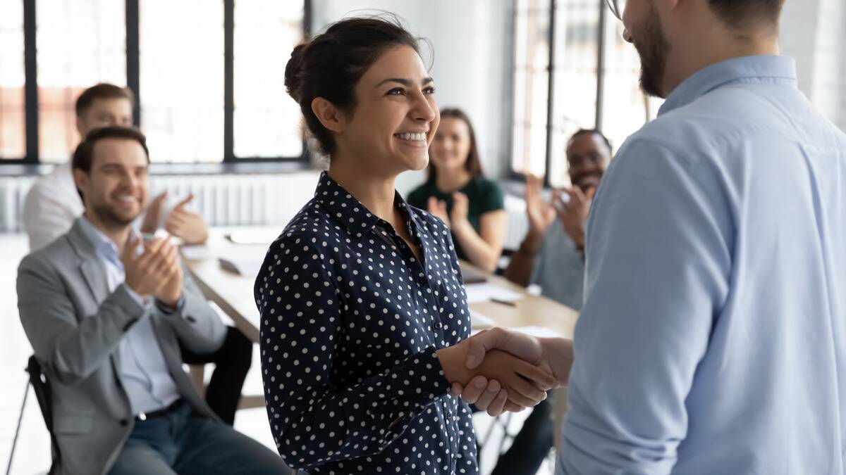 A woman and his boss shaking hands as she's being given a promotion.