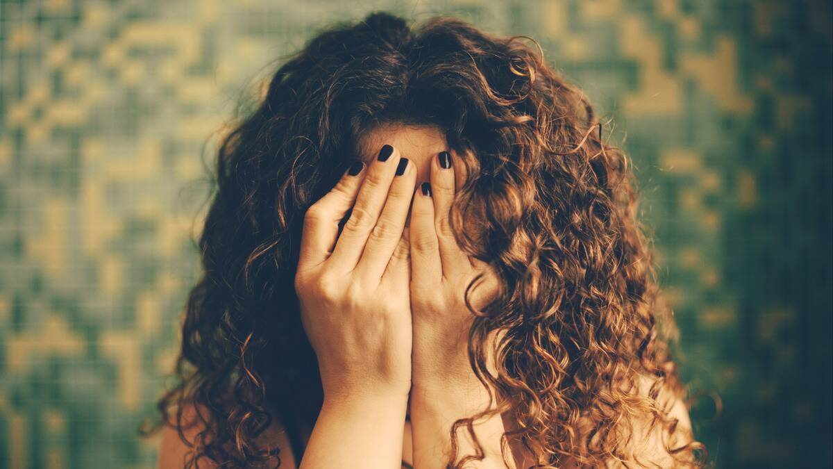 A woman with large, curly hair covering her face with her hands.