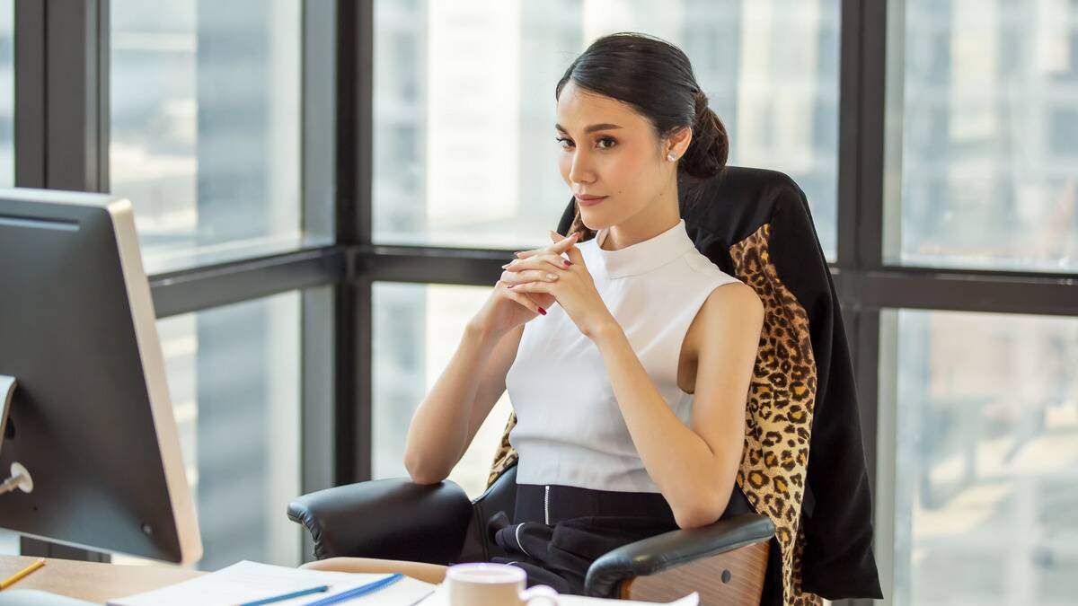 A woman, clearly a boss or manager of some kind, sat at her desk with her hands together, looking content and thoughtful.