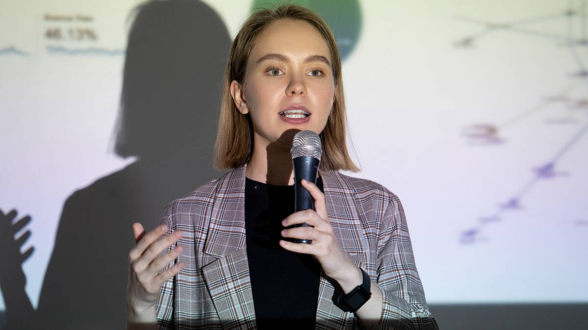 A woman giving a presentation, the powerpoint shining on her face as she speaks.