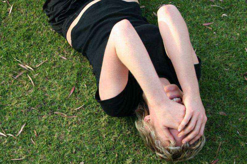 A woman laying on her back in the grass, hands covering her face.