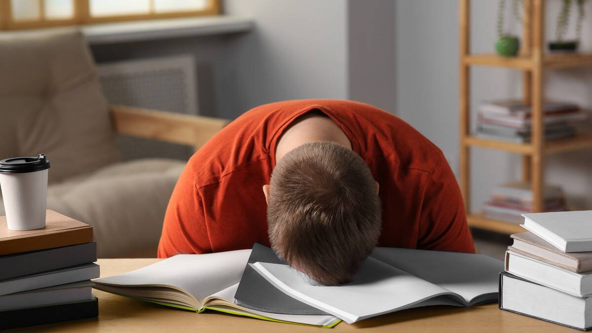 A man asleep face down on his desk, atop a few open notebooks.