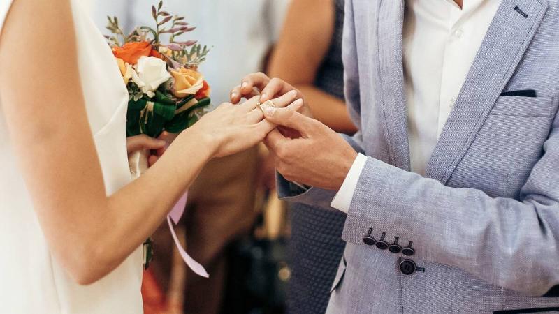 A close shot of a couples hands as they're getting married, the groom putting a ring on the bride's finger.