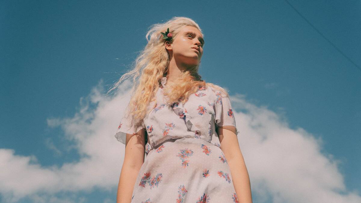 A low-angle shot of a woman standing beneath a vibrant blue sky.