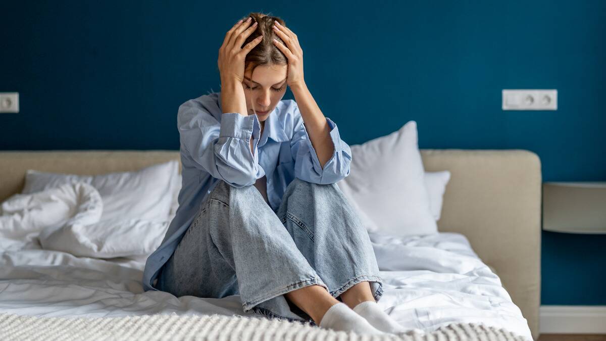 A woman sitting in bed, knees drawn up, head in her hands.