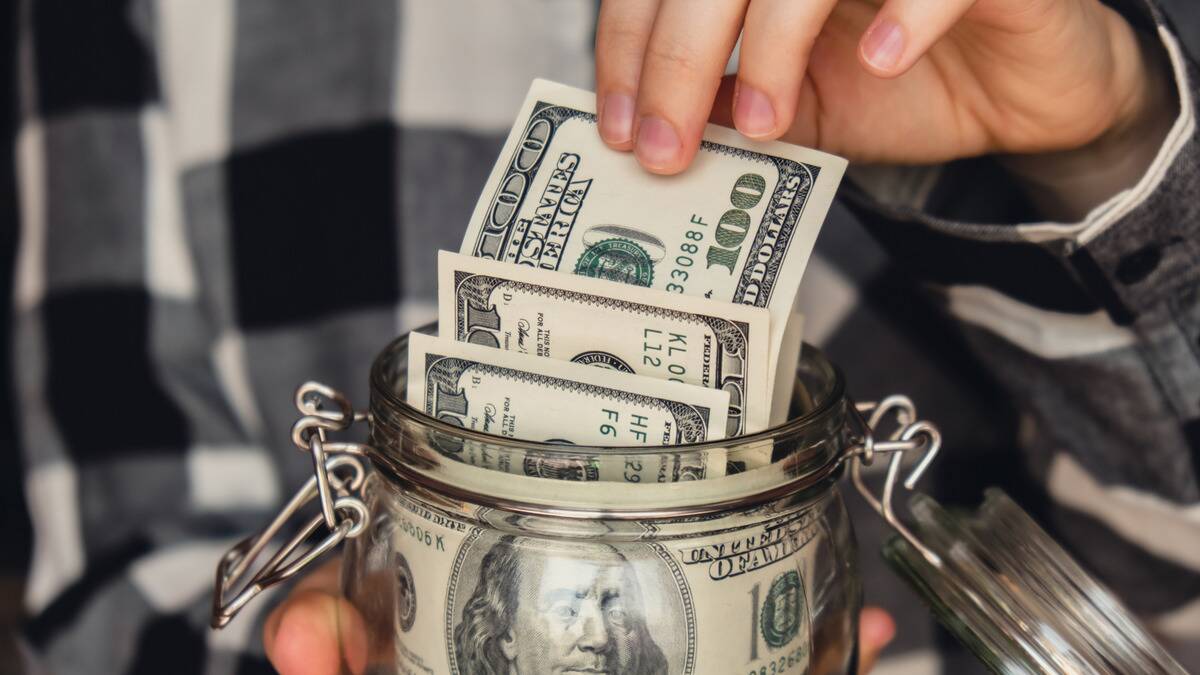 A close shot of someone pulling a $100 bill from a jar full of $100 bills.