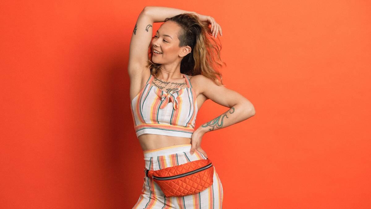 A woman in a colorful outfit in front of an orange backdrop, posing and smiling confidently.