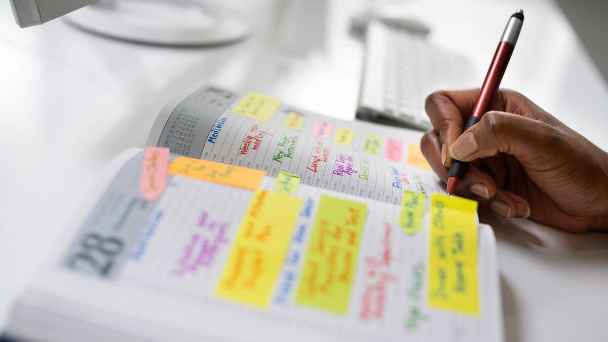 A side shot of someone writing in a planner, with it being visibly full of events and plans.