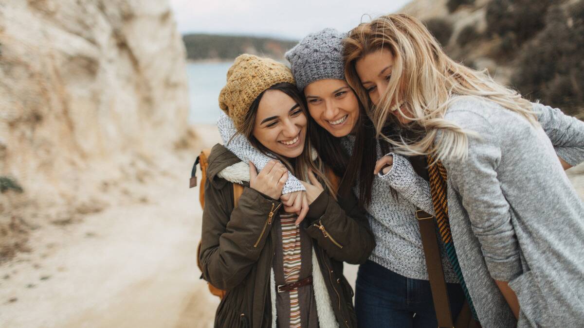 Three friends all walking with their arms around one another, smiling.