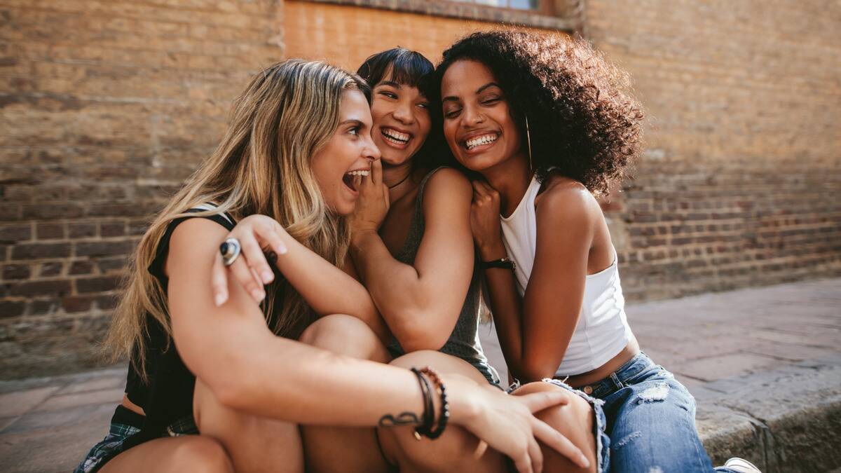 Three friends all sitting close and embracing one another, all smiling.