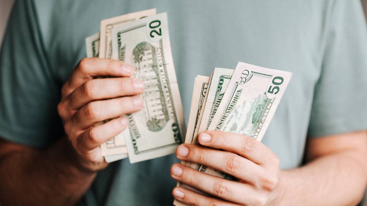 A close shot of a pair of hands counting a stack of $20 bills in front of their chest.