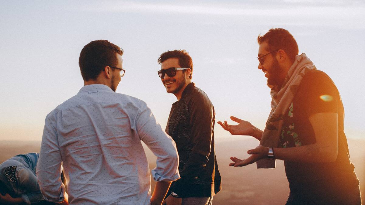 A group of three friends walking outside during sunset, smiling as they chat.