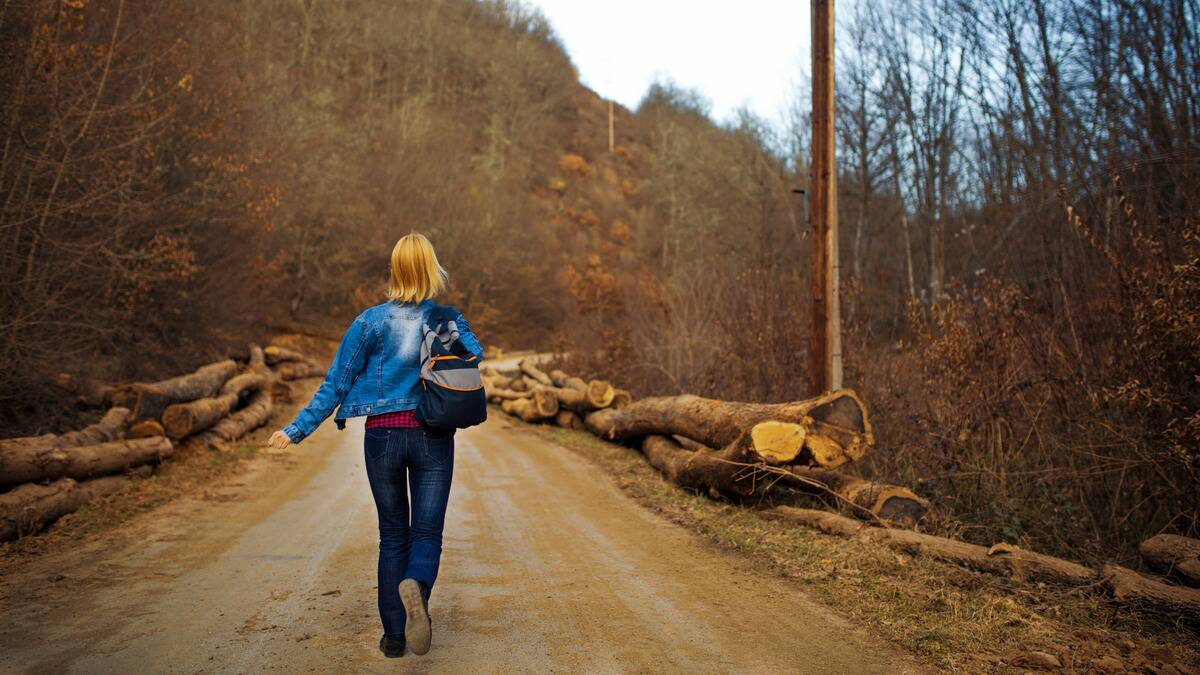 A woman running away from the camera down a dirt road toward a wooded area.