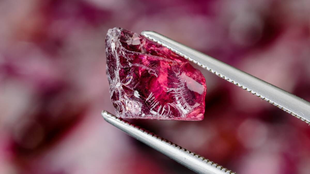 A piece of raw garnet being held between tweezers