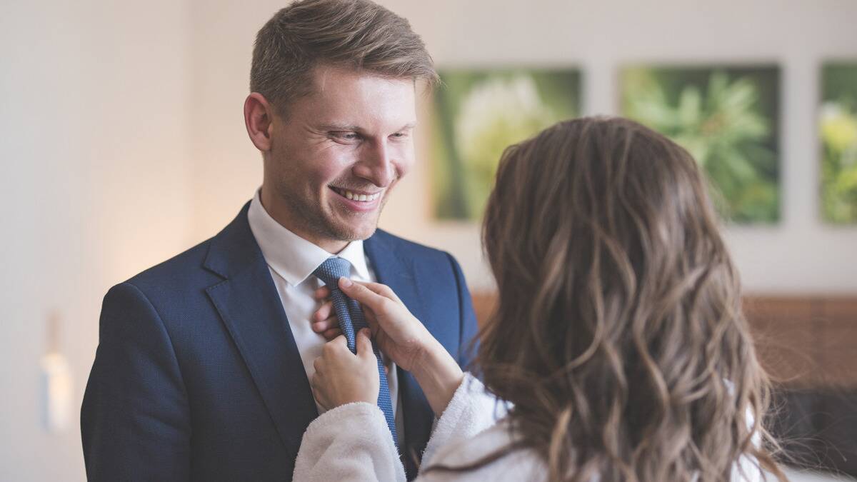 A man smiling at his wife as she puts his tie on.